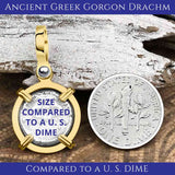 A gold-framed ancient Greek Gorgon silver Drachm coin pendant lies beside a U.S. dime on a textured surface. Text overlay on the coin pendant reads: "SIZE COMPARED TO A U.S. DIME."